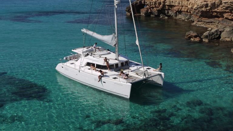 Katamaran Atlantis vor Anker in einer türkisfarbenen Bucht. Einzigartiges Yachtcharter-Erlebnis auf Ibiza.