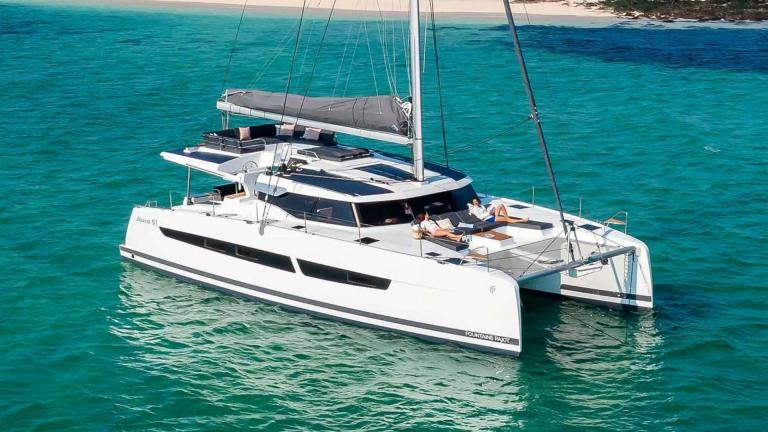 The catamaran Kebisiks is anchored in turquoise water as guests sunbathe on the bow.