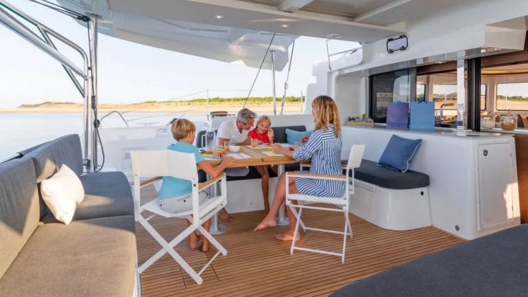 Children and their parents sit at a table on the deck of the catamaran Shanti.