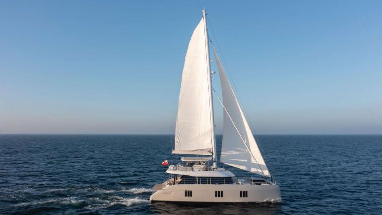 The catamaran Spice of Life glides under sail on blue waters near Athens.