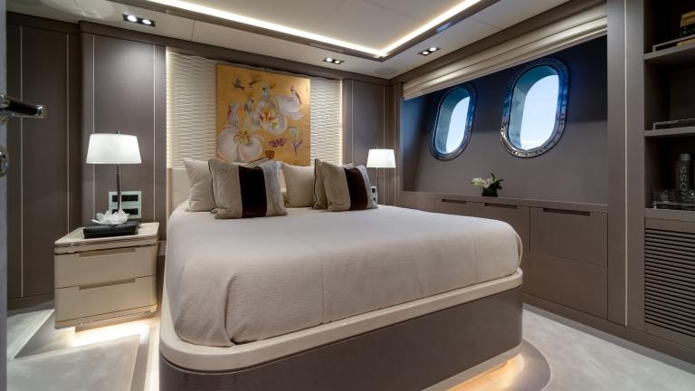 Elegant bedroom on the yacht with luxurious bed, art on the wall and sea view through two porthole windows.