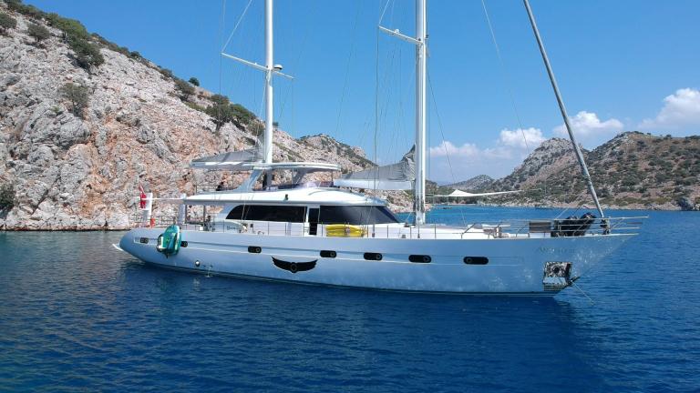 Motorsailer Angelo 3 anchored in a picturesque bay with rocky scenery in the background.