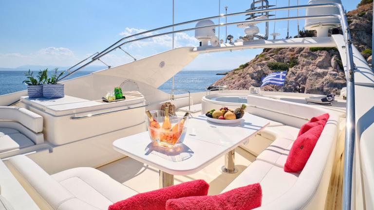 Elegant dining area on the flybridge of a motor yacht with views of rocky coastline and turquoise water
