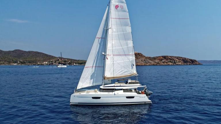 Helidoni charter catamaran sails smoothly off the coast of Volos with full sails.