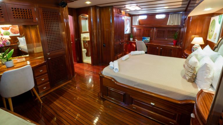 The main cabin of the Gulet Elianora has elegant wooden walls, a large bed, a desk, a cosy seating area and a private ba
