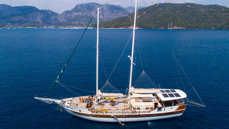 The gulet yacht Amazon Solo sails in the calm waters off the coast of Göcek, surrounded by green hills and clear blue sk