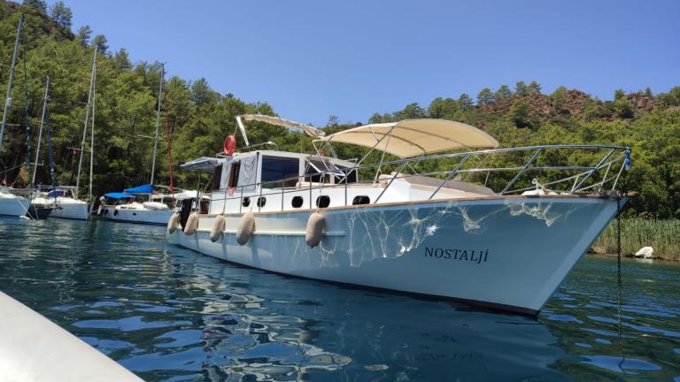 Gulet Nostalji anchored in Göcek, surrounded by clear waters and green hills.