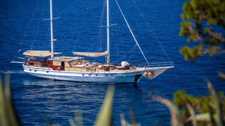 A luxurious gulet sails in turquoise waters surrounded by lush vegetation.