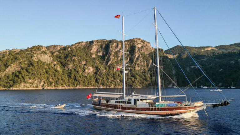 Die Gulet Tarkan 5 segelt vor der Küste von Fethiye, mit grünen Hügeln im Hintergrund und einer türkischen Flagge am Hec