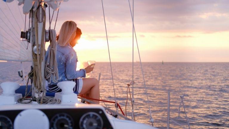 Ein Paar trinkt ein Glas Weißwein auf einem Boot bei Sonnenuntergang.