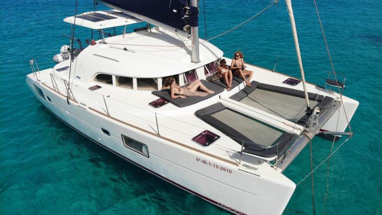 Guests sunbathe on the foredeck of catamaran New Tribe, enjoying the turquoise sea.