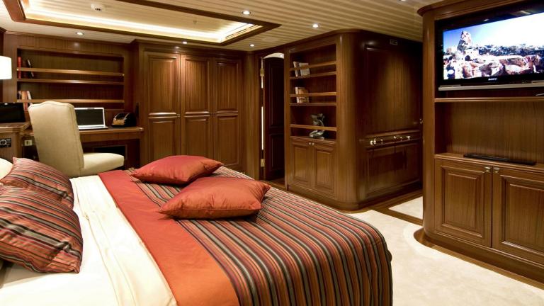 A spacious gulet bedroom in a wooden style. You can see the TV is on