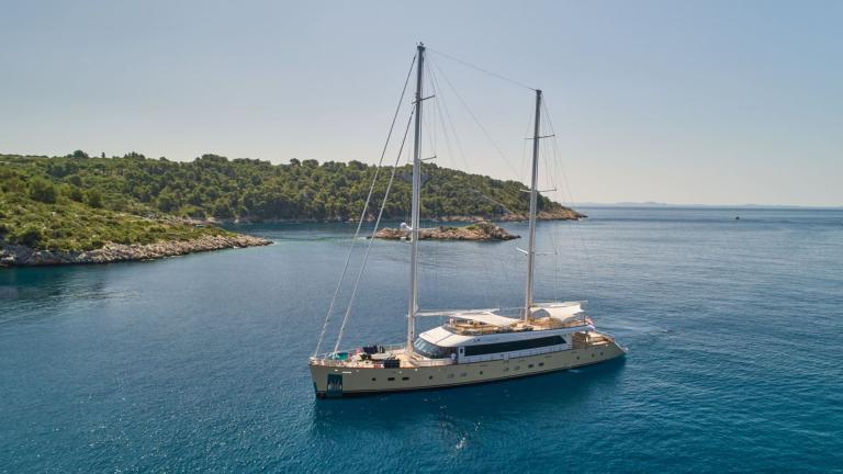 An elegant motor sailor anchored in a picturesque, tranquil bay under bright sunshine.