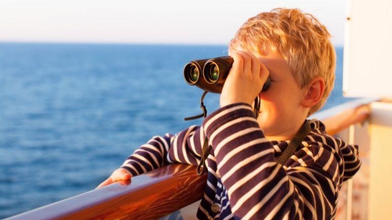 While on a blue cruise, a little boy watches the routes with binoculars.