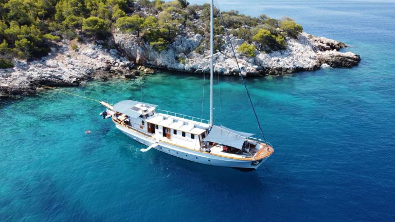 Cosmos is anchored in crystal-clear waters with a rocky, green island in the background.