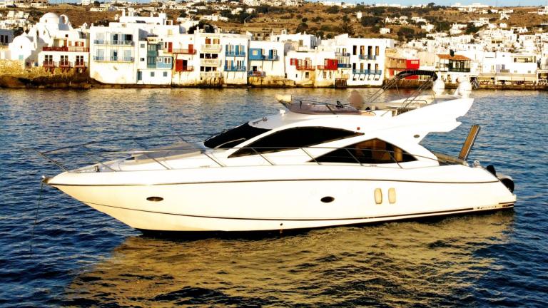 Die weiße Motoryacht liegt ruhig vor den farbenfrohen Häusern von Mykonos.