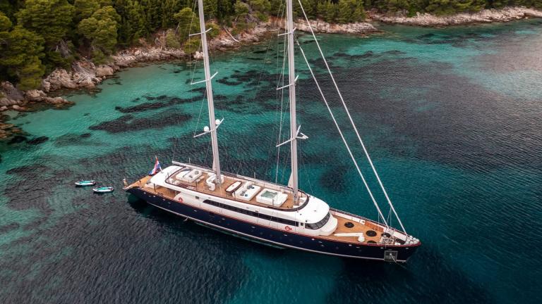 The luxurious Motor Sailor Nocturno anchored in turquoise waters off a green coastline.