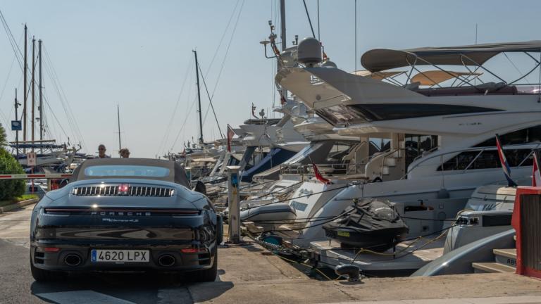 Porsche Carrera 4S parkt in einem Yachthafen neben vielen edlen Yachten
