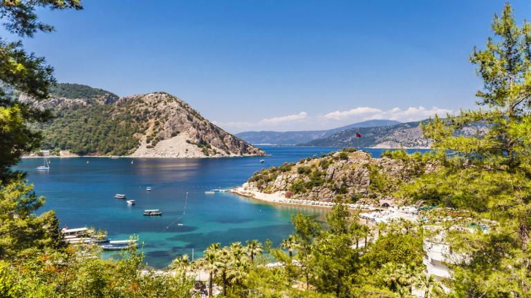 A serene view of Turunç Bay in Marmaris, Turkey, surrounded by lush greenery and rugged mountains. Clear turquoise waters invite visitors for a peaceful holiday escape in Marmaris, Turkey