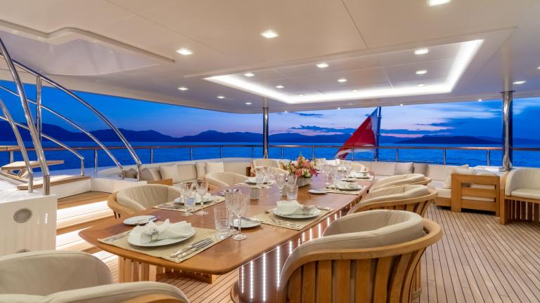 Elegant dining table on the yacht, set for dinner, with a view of the sea at sunset.
