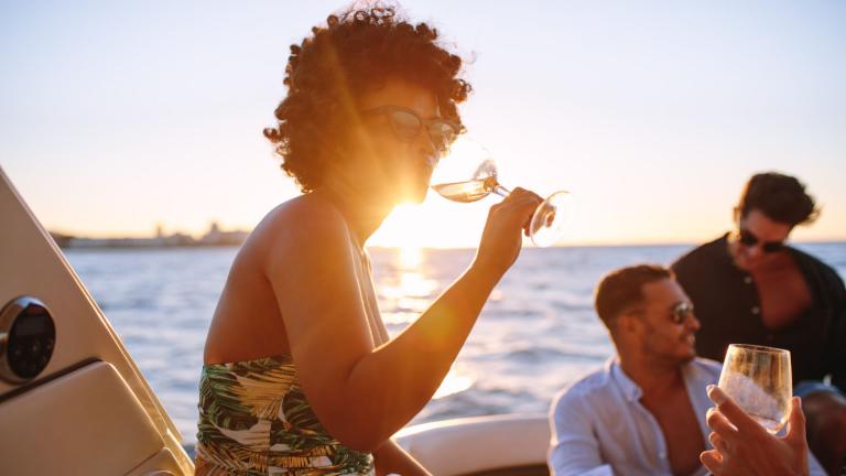 Frau mit Sonnenbrille trinkt Wein auf einer Yacht während eines Sonnenuntergangs auf einer Motoryacht