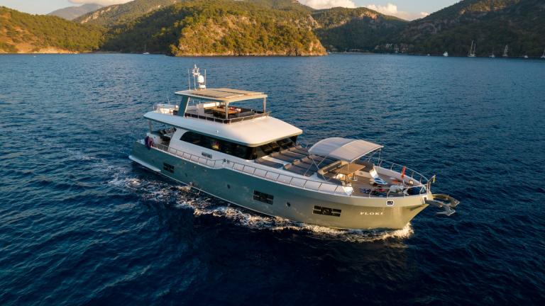 The Floki trawler yacht elegantly glides through a tranquil bay in the evening light.