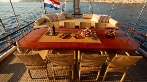 Deck der Gulet Malena mit Esstisch und kroatischer Flagge, umgeben von Wasser und Küste in Split, Kroatien.