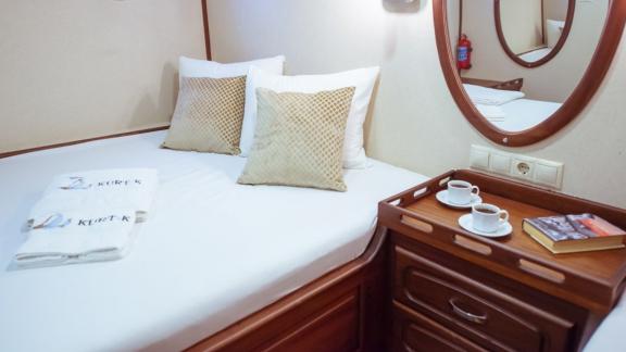 A cosy bed in a cabin on a sailing boat with a bedside table holding two cups of coffee.