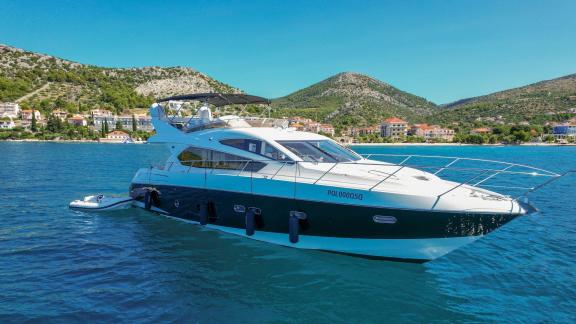 The yacht 2 Drunk is anchored near the coast, with mountains visible in the background.
