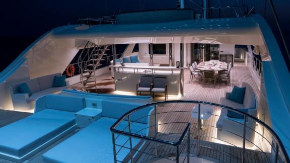 Illuminated upper deck of the Meira sailing yacht at night with cozy seating and dining area.