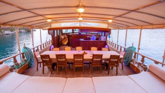 Covered dining area of a sailing boat with a large table and chairs.