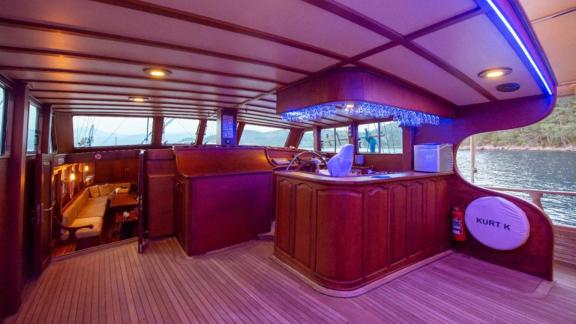 Interior wheelhouse of a luxury sailing boat with wood panelling and blue accent lighting.