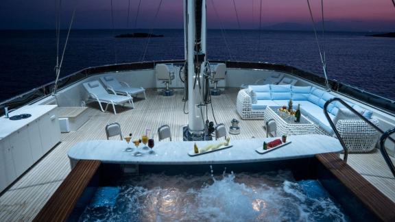 Relax in the illuminated jacuzzi and stylish lounge of the Meira sailing yacht with nighttime sea views.