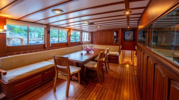 An elegant dining area inside a sailing boat with wooden furniture and large windows.