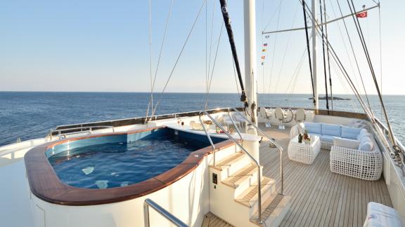 The deck of the Meira sailing yacht features an elegant pool and a white lounge area with sea views.