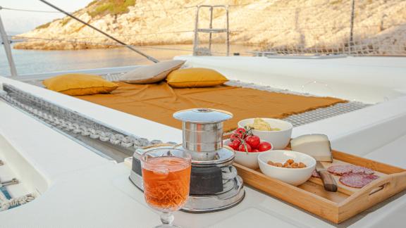 Köstliche Snacks und ein erfrischender Drink auf dem Trampolin des Katamarans Marla Lagoon 450F, perfekt zum Entspannen.