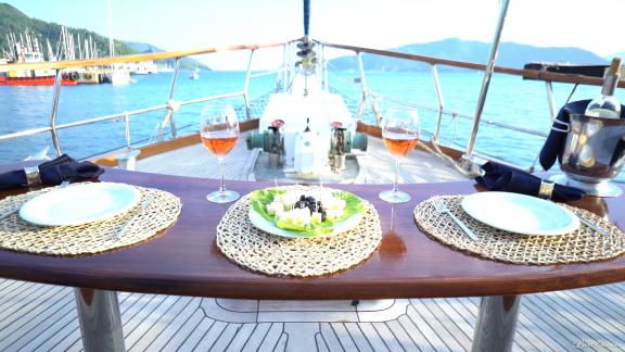 A set table with wine glasses and appetizers on the deck of a gulet in a scenic setting.