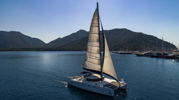 The Big Easy catamaran sails in a calm bay with green mountains and blue sea in the background.