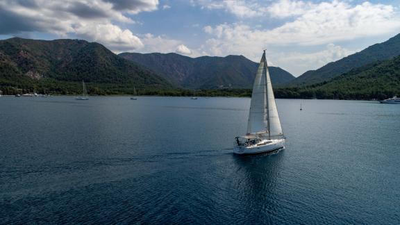 The sailing yacht Zezo glides on calm waters, with mountains visible in the background.