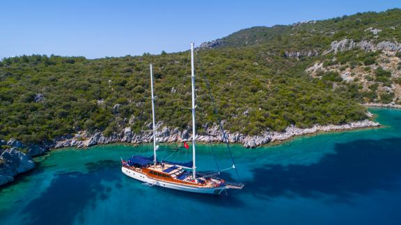 The SY Voyage gulet anchored in a picturesque, turquoise bay with green hills in the background.