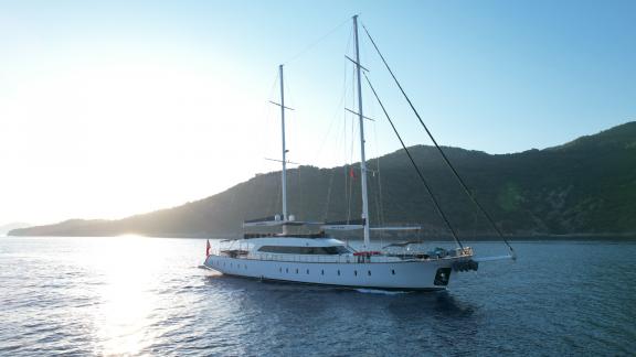 Elegante Segelyacht auf ruhigem Wasser bei Sonnenuntergang, umgeben von grünen Hügeln in Göcek.