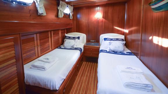 A cosy cabin on the Gulet Ros Mare with wooden furnishings and two single beds.