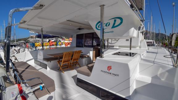 The spacious aft deck of the Coco D catamaran offers comfortable seating areas and a dining table.