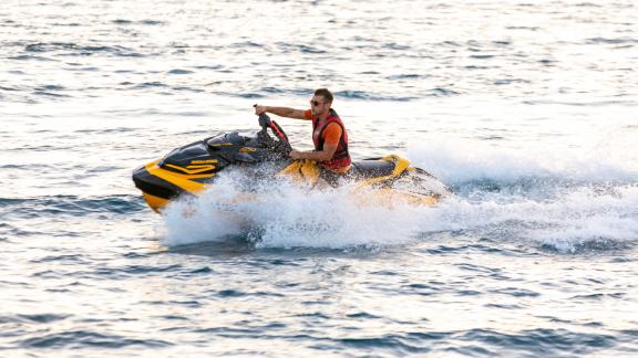 A man in a lifejacket steering a yellow jet ski. Splashing in all directions
