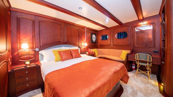 The master cabin of SY Voyage with a large bed, elegant wood decor, and a cozy sofa.