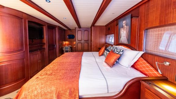 Die Hauptkabine der SY Voyage mit einem großen Bett, Fernseher und eleganter Holzausstattung.