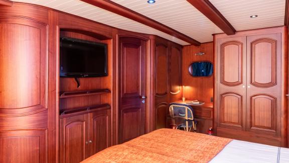 Master cabin of SY Voyage with a large bed, television, and a cozy desk area.