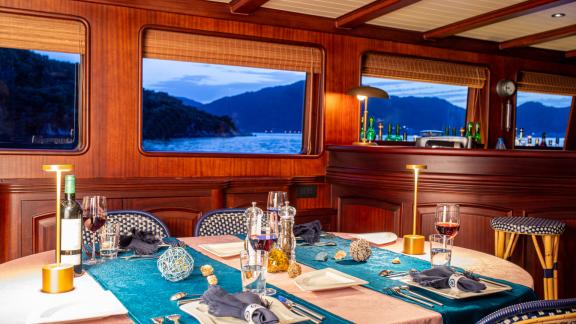 Stylishly set table for dinner in the salon of SY Voyage with a view of the sea.