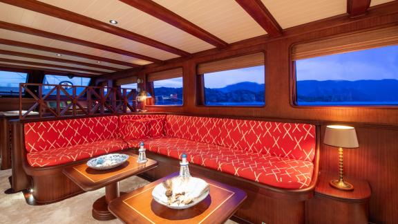 The lounge in the salon of SY Voyage with a large red couch and a sea view.