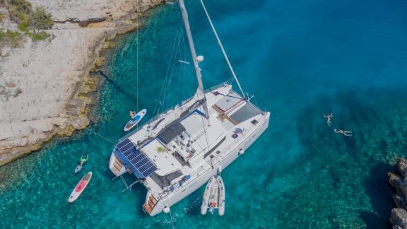 A catamaran is anchored in a secluded bay with clear turquoise waters along the Adriatic coast.